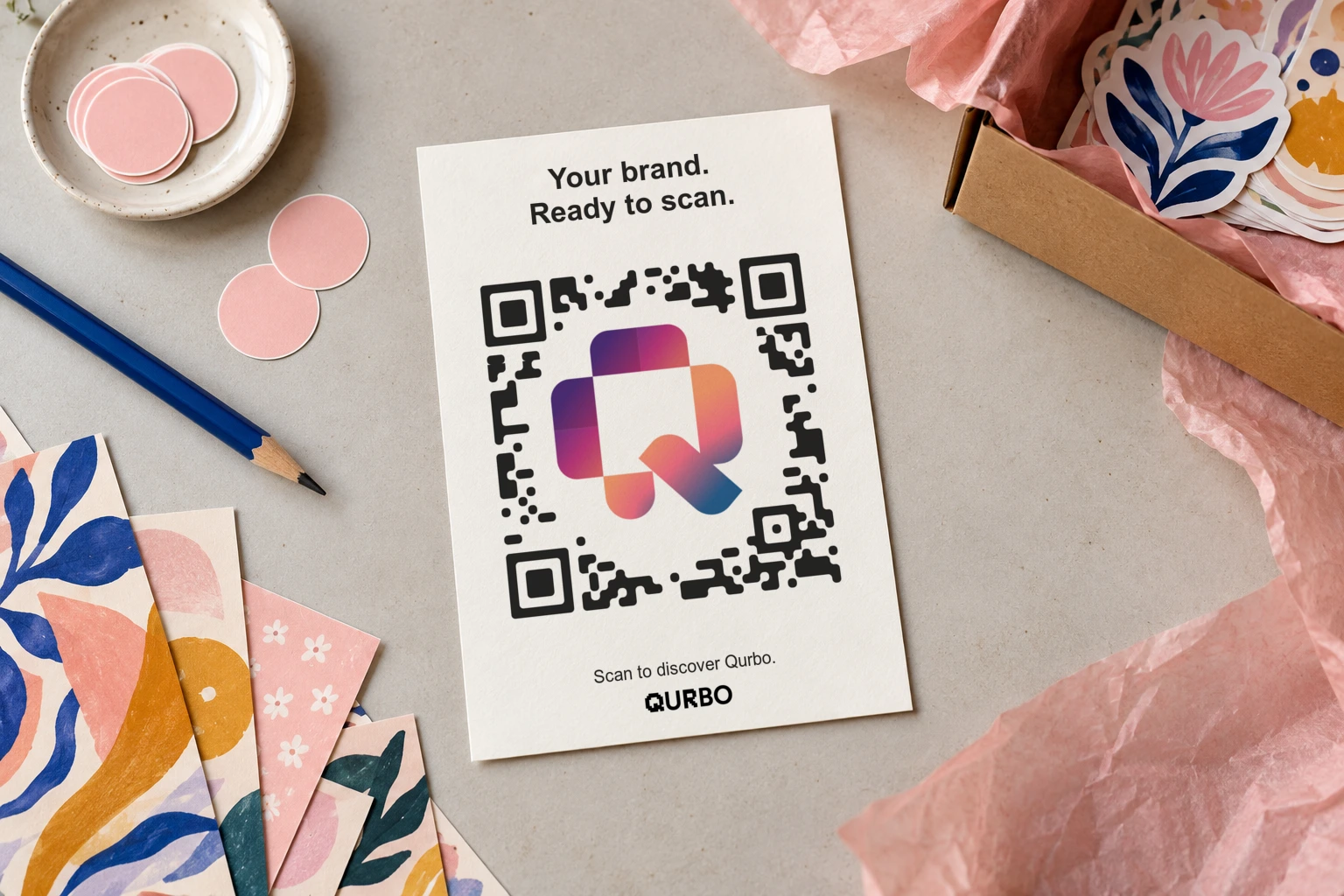 Cream card mockup among floral paper and pink tissue, showing Qurbo’s logo QR and the words Scan to discover Qurbo.